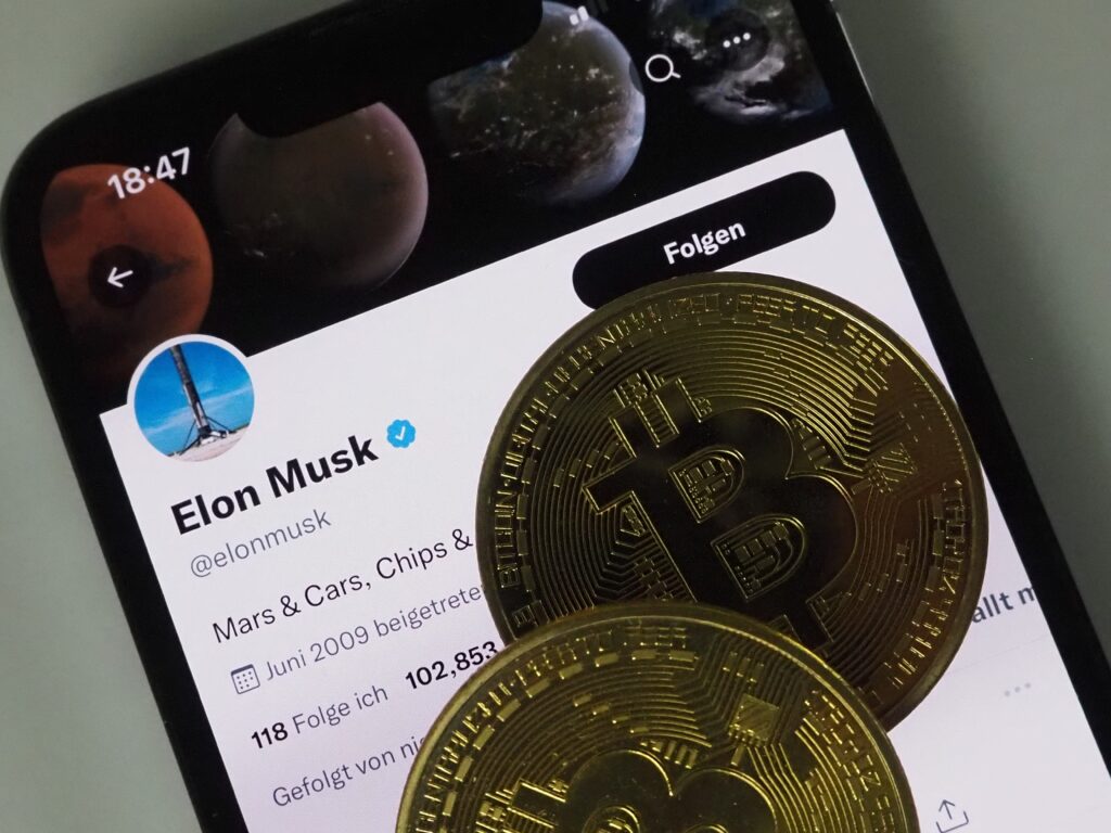 mobile phone with Elon Musk name on screen with 2 bitcoin coin on top