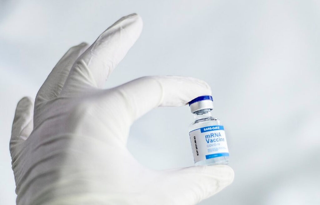 Image of gloved hand holding a vial of mRNA vaccine.