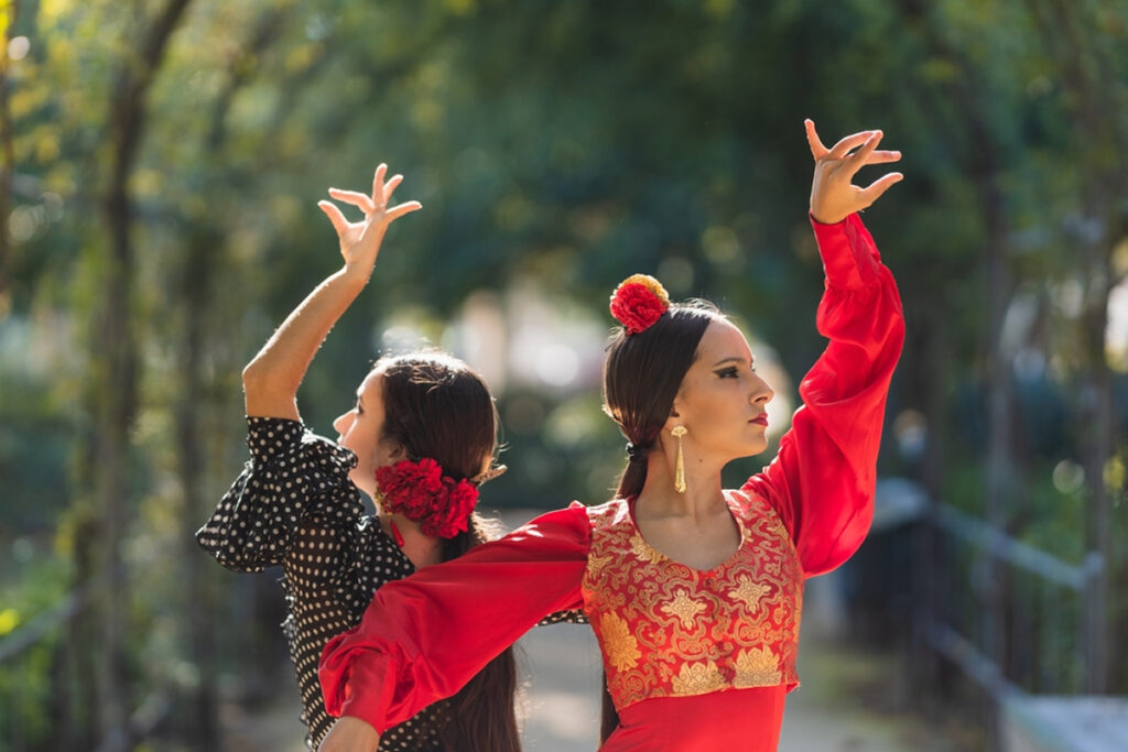Image of two women dancing in traditional flamenco costumes.
