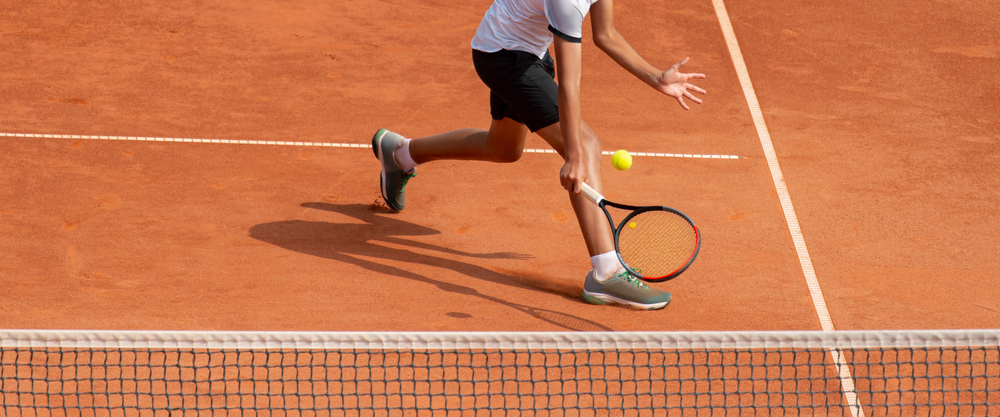 Clay tennis court with a player coming into the net about to do a back hand shot