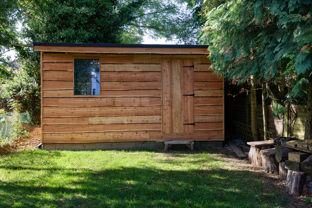 A wooden garden shed at the end of the garden with a small grass area out front