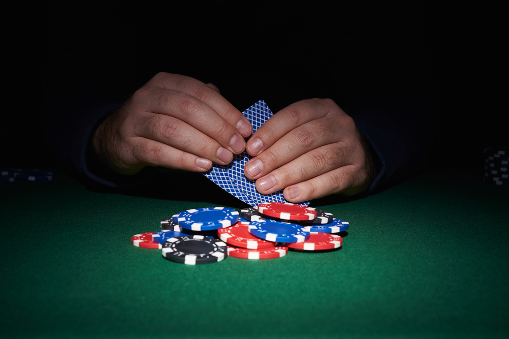 view of a mans hands holding playing cards with poker chips in front of him