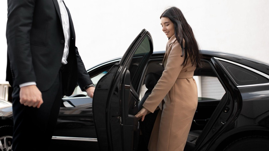 Chauffeur holding the door open to luxury car with young woman getting in