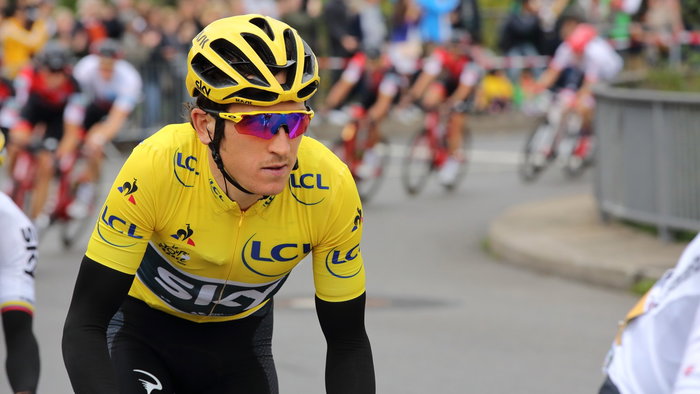 Geraint Thomas wearing the yellow jersey during the Tour de France, focused as he rides with the peloton in the background