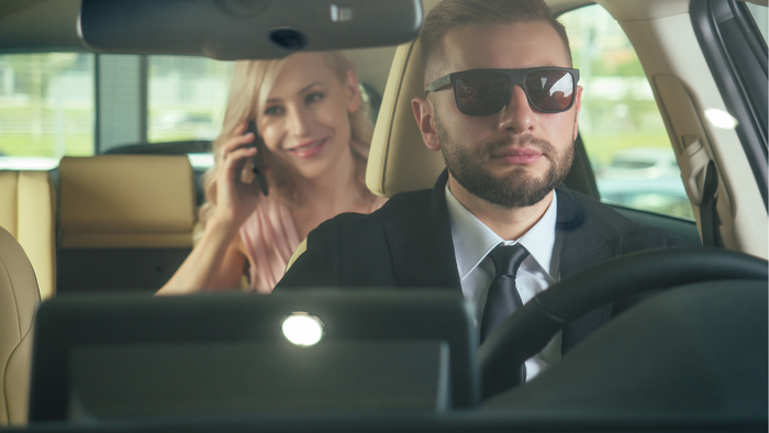 Driver in suit and sunglasses with female passenger in back seat of car