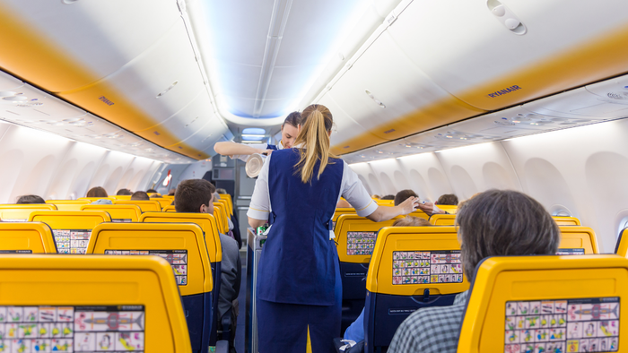 Ryanair flight attendants serving passengers inside a plane with yellow seat backs