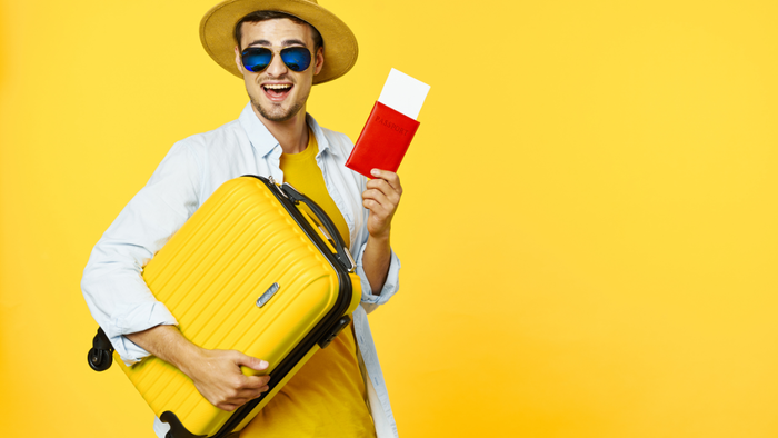 Smiling man holding yellow suitcase and passport against yellow background