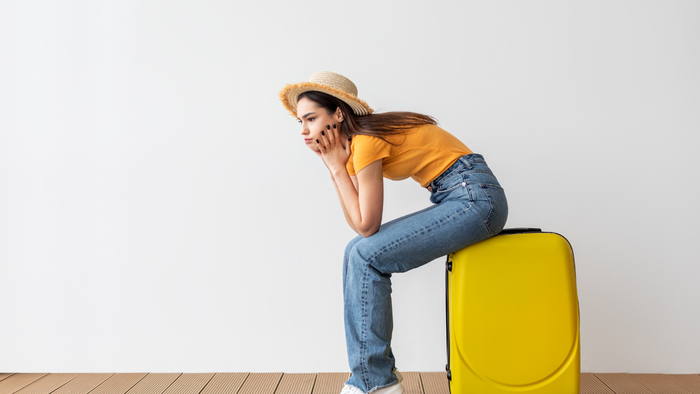 Frustrated female traveller sitting on a yellow suitcase indoors