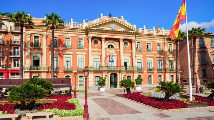 Murcia City Hall with palm trees and Spanish flag in front.
