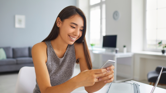 Woman smiling while using smartphone at home workspace.