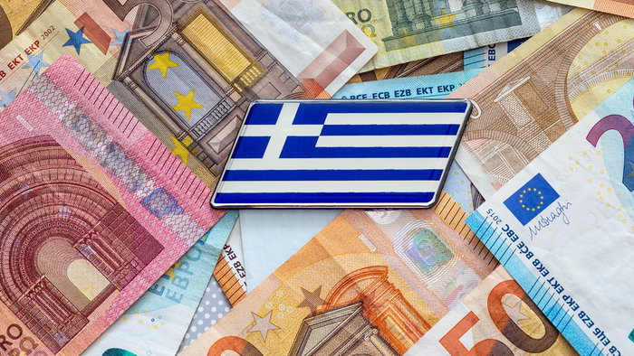 Greek flag badge placed on a spread of euro banknotes.