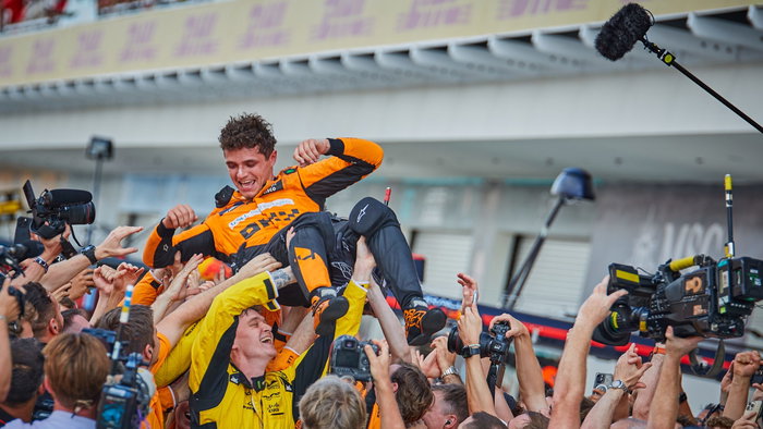 Lando Norris being lifted up by his team after winning