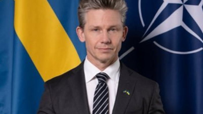 Pål Jonson standing in front of the Swedish and NATO flags during a security briefing.