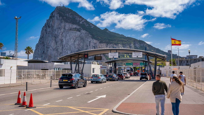 Gibraltar Spain border crossing at La Línea with cars passing through checkpoints beneath the Rock of Gibraltar on a clear day.
