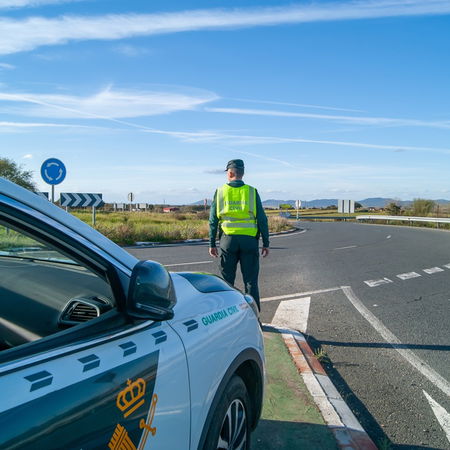 Guardia Civil traffic officer standing beside a patrol car on a Spanish road during a traffic control operation.