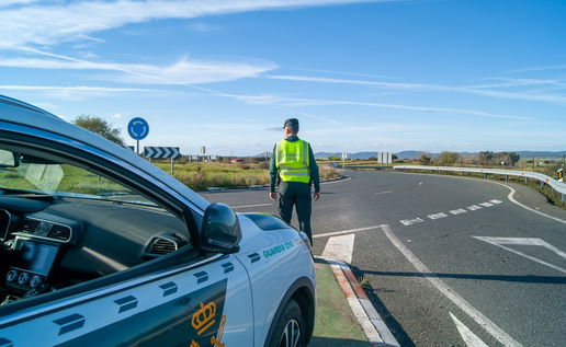 Guardia Civil traffic officer standing beside a patrol car on a Spanish road during a traffic control operation.