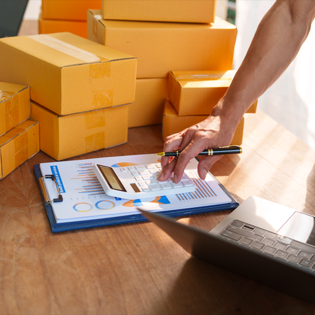 Man using a calculator with boxes next to him and a laptop
