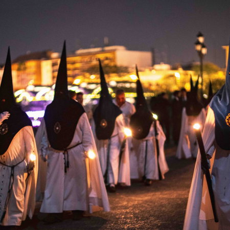 Semana Santa procession at night in Andalucía with penitents in traditional robes and candles