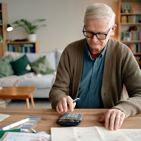 Retired man in Spain checking documents and calculating his pension payments at home.