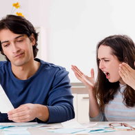 Couple at home looking stressed while reviewing bills and paperwork at a table