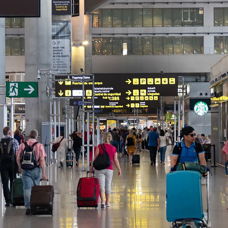 Passengers walking through a busy European airport departure hall with luggage