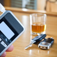 Hand holding a breathalyser device next to a glass of alcohol and car keys on a table