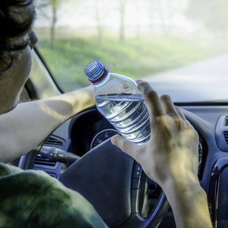 Driver holding a water bottle while driving a car in Spain, illustrating potential distraction behind the wheel