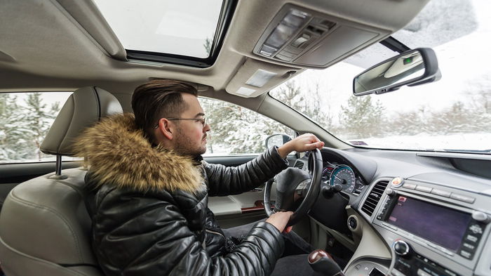 Driver wearing a thick winter coat while driving a car in cold weather