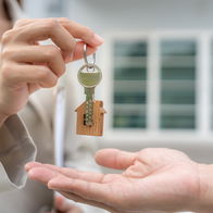 Real estate agent handing over house keys to a new homeowner in front of a property.