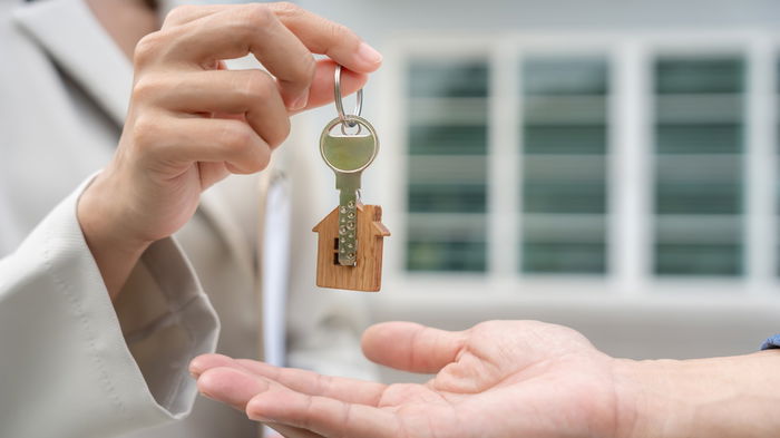 Real estate agent handing over house keys to a new homeowner in front of a property.