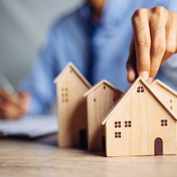 Person placing a miniature house model on a table, representing housing and property market decisions in Europe