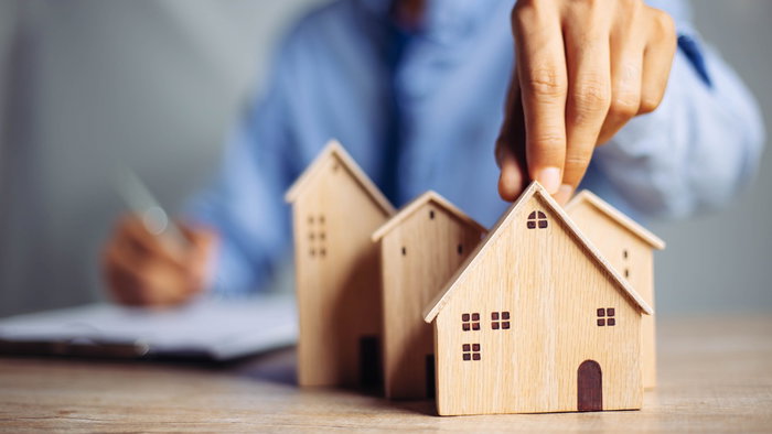 Person placing a miniature house model on a table, representing housing and property market decisions in Europe