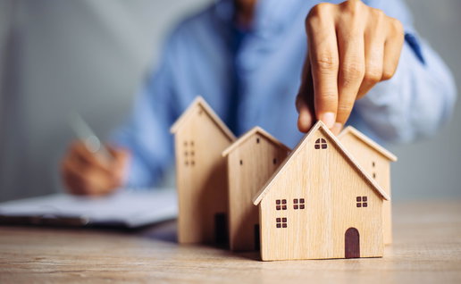 Person placing a miniature house model on a table, representing housing and property market decisions in Europe