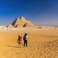 Tourists standing in the desert facing the Pyramids of Giza in Egypt under a clear blue sky.