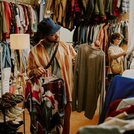 Person browsing racks of clothing in bright thrift store with various garments on display during daylight Peering at different shirts and examining styles and options