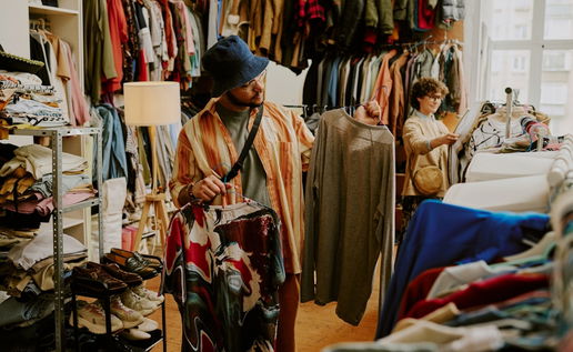 Person browsing racks of clothing in bright thrift store with various garments on display during daylight Peering at different shirts and examining styles and options