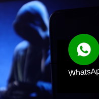 WhatsApp logo on a smartphone with a blurred hacker figure in the background