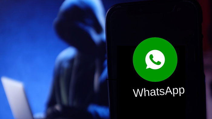 WhatsApp logo on a smartphone with a blurred hacker figure in the background