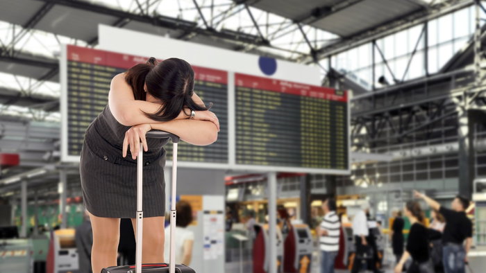 Frustrated traveller leaning on suitcase at airport departures board after a cancelled flight