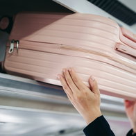 Person putting their carry-on bag in the overhead locker on an airplance