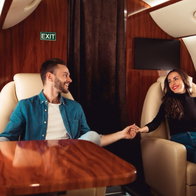 Charming couple sat on a private jet holding hands across the ailse