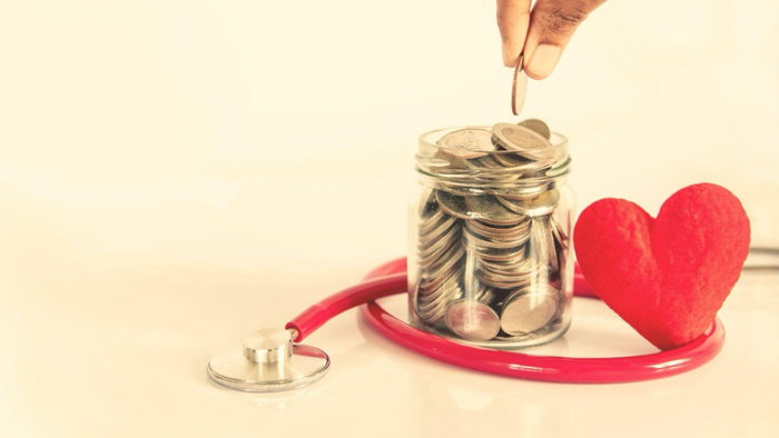 A jar with money in with someone adding to it and a red stethoscope around the bottom of the jar