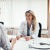 Blonde general practitioner holding eyeglasses while talking to a female patient.