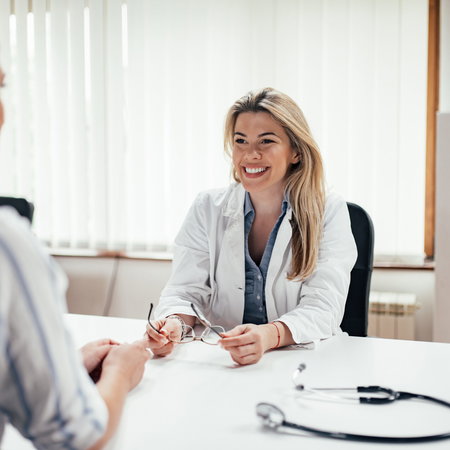 Blonde general practitioner holding eyeglasses while talking to a female patient.