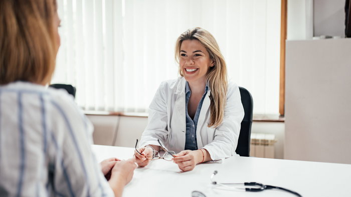 Blonde general practitioner holding eyeglasses while talking to a female patient.