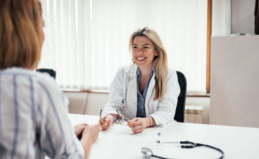 Blonde general practitioner holding eyeglasses while talking to a female patient.