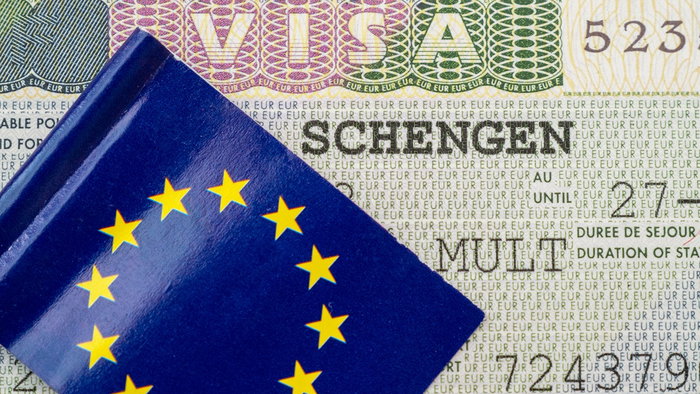 Schengen visa sticker inside a passport with EU flag cover visible