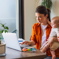 Woman working at home on a a laptop holding a young child