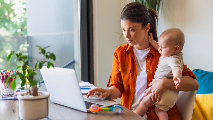 Woman working at home on a a laptop holding a young child