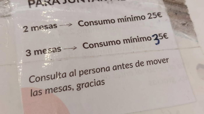 Sign at a Spain café terrace stating customers must meet a minimum spend to join tables together
